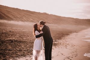 A couple embraces on a serene beach at sunset, with waves gently lapping at the shore.