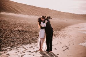 A couple embraces on a serene beach at sunset, leaving footprints in the sand as waves gently roll in.