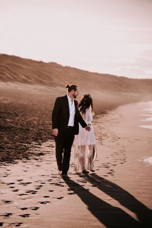 A romantic couple walking on a sandy beach leaving footprints behind them at sunset.