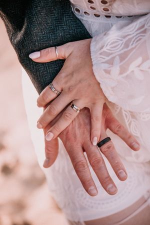 Close-up of hands wearing wedding rings against white lace and dark fabric.