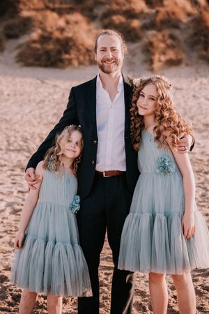 Family portrait series at sunset with children wearing matching blue tulle dresses on the beach.