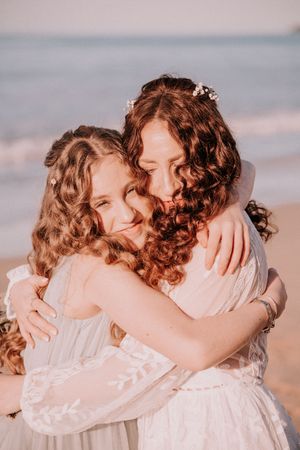 Series of intimate embraces between siblings wearing white dresses on a beach at sunset.