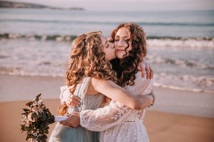 A couple shares an intimate moment on a sandy beach with waves crashing in the background.