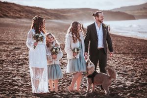 A wedding group stands together on a sandy beach during golden hour.