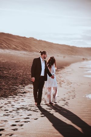 A couple walking along a sandy beach leaving footprints during a sunset photo session. Editorial Couples Portraits in Gwithian, Cornwall.