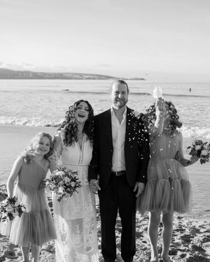 A black and white beach wedding portrait with a bridal party holding bouquets during the confetti moment.