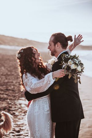 A joyful wedding moment captured on the beach with the couple laughing and embracing.