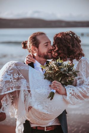 Romantic beach wedding photos with couple holding bouquets against ocean backdrop.