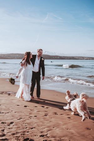 A couple walks along the beach with their dogs during their wedding photoshoot.
