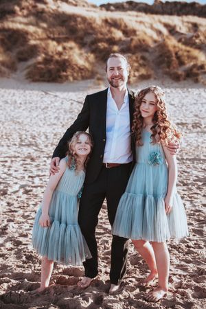 Family portrait on beach with people wearing coordinating blue dresses and formal wear.
