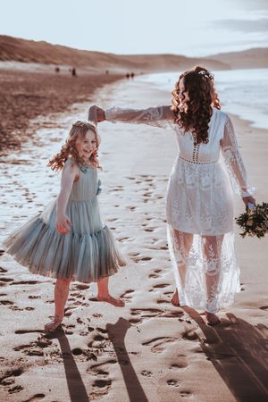 People in flowing dresses dancing and twirling on beach at sunset.