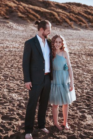 Wedding party members pose on a sandy beach at golden hour.