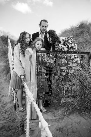 Black and white photo of wedding party by rustic fence with photo display on beach.