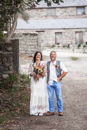 Couple in white dress and casual attire poses on rustic path near stone building.