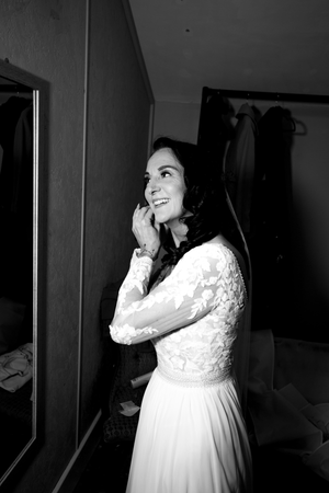 A person in a white lace wedding dress smiles joyfully while getting ready.