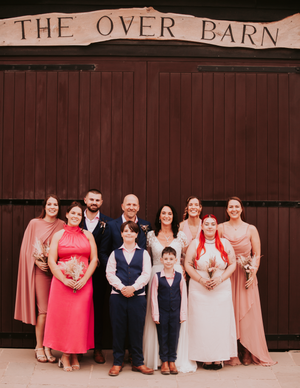 Wedding party poses in front of The Over Barn sign wearing coral and navy attire.Over Barn, Gloucester,