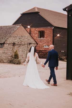 Newlyweds walking together outside rustic brick and stone barn buildings. Over Barn, Gloucester,