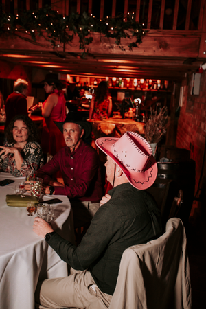 Wedding guests enjoying themselves at tables during an evening reception with red ambient lighting.Direct Flash, Over Barn, Gloucester,