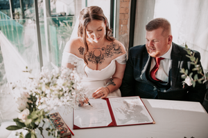 Signing of wedding documents during an intimate ceremony with white floral arrangements.