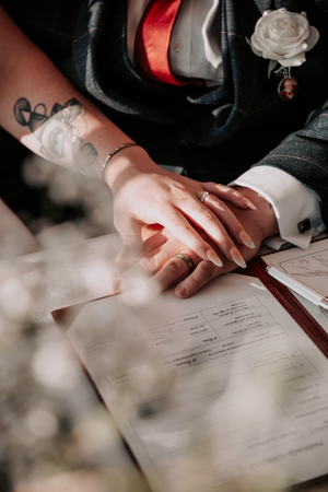 Close-up view of hands signing marriage certificate with red ribbon detail.