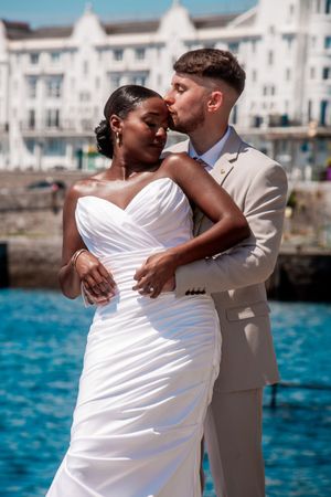 A couple shares an intimate moment by a seaside harbor during their wedding celebration.