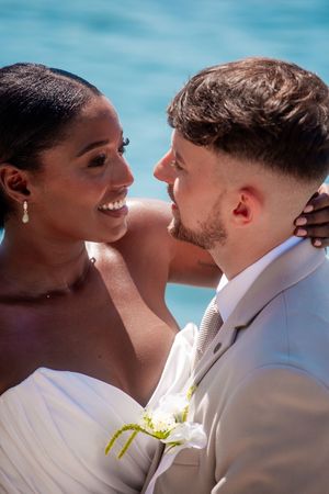A couple shares an intimate moment against a bright blue ocean backdrop.