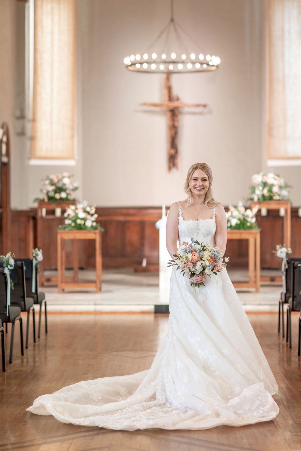 A beautiful white wedding gown with a long train photographed in a NASHVILLE church sanctuary with floral arrangements and a chandelier.