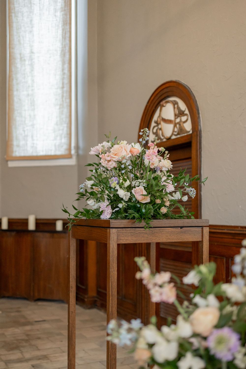 Delicate pink and white floral arrangements in wooden stands line a church aisle with natural light streaming through windows. NASHVILLE WED