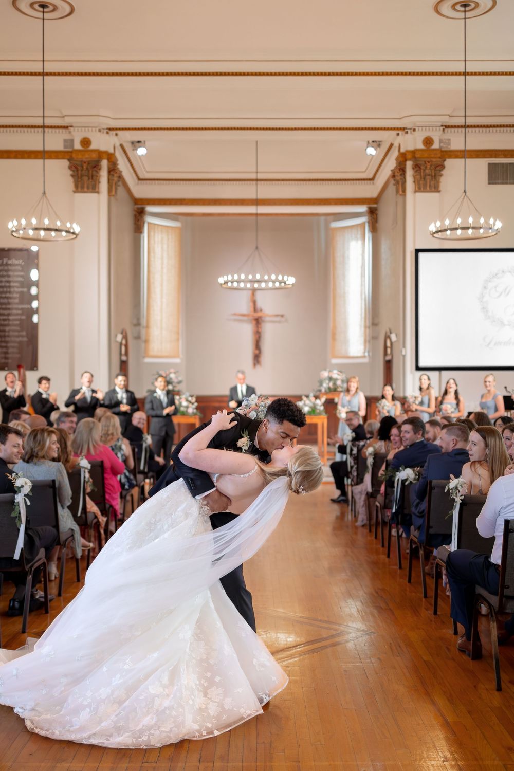 Wedding guests raise their hands in celebration as a couple dances in a church reception hall with hardwood floors.  NASHVILLE WEDDING PHOTO