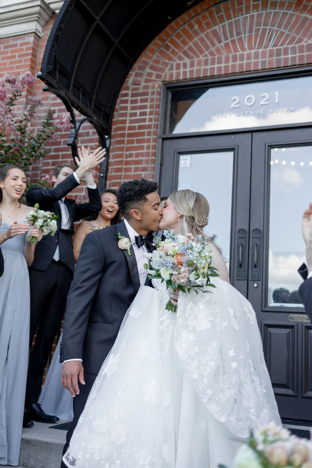 Joyful wedding celebration outside a brick building with newlyweds and wedding party in black and gray attire.  NASHVILLE WEDDING PHOTOGRAPH