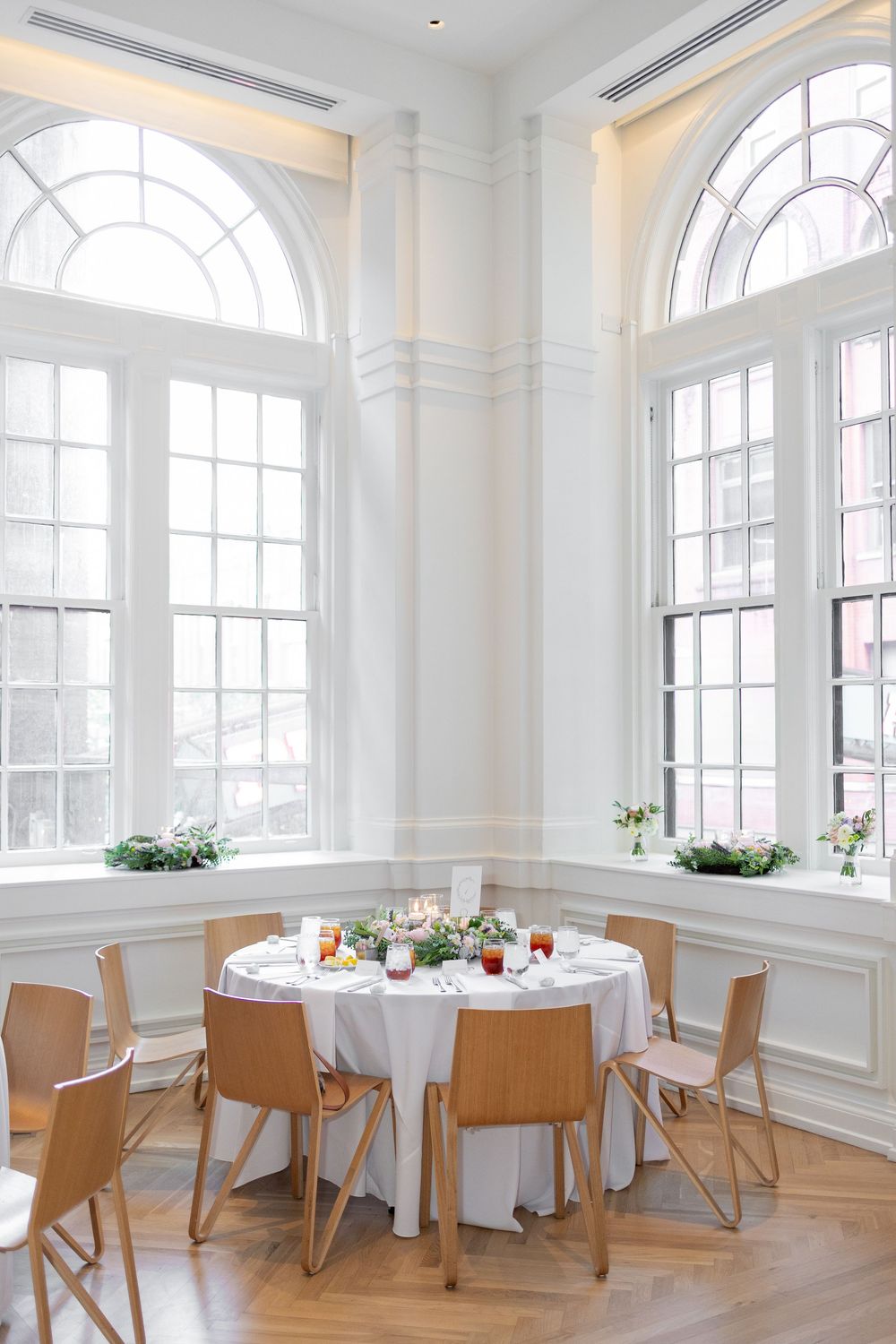 Bright sunlit event space with arched windows, white walls, and round dining tables set for a formal occasion. NASHVILLE WEDDING PHOTO