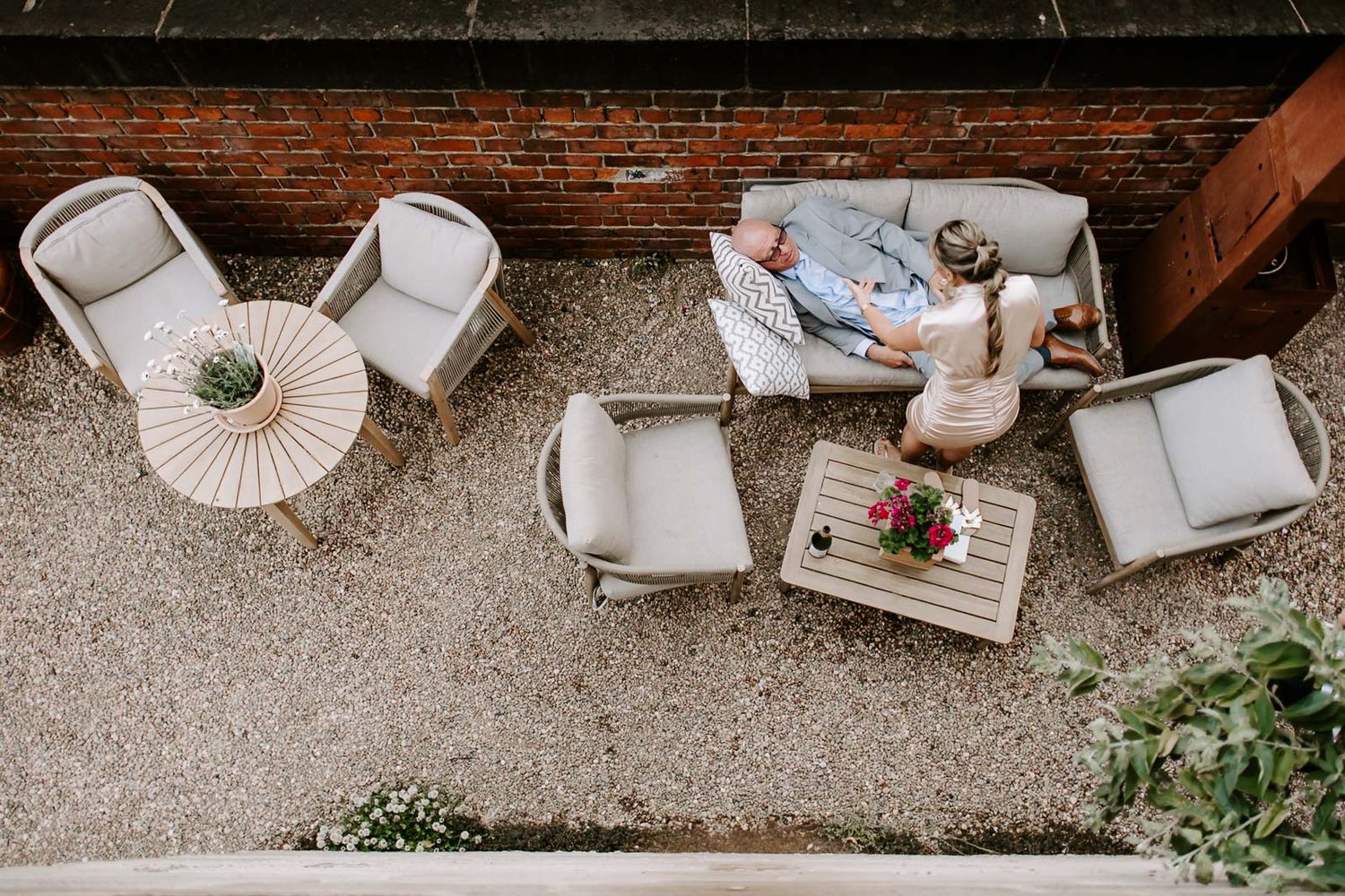 Aerial view of a cozy outdoor patio setup with white chairs and decorative items on a concrete surface next to brick wall.