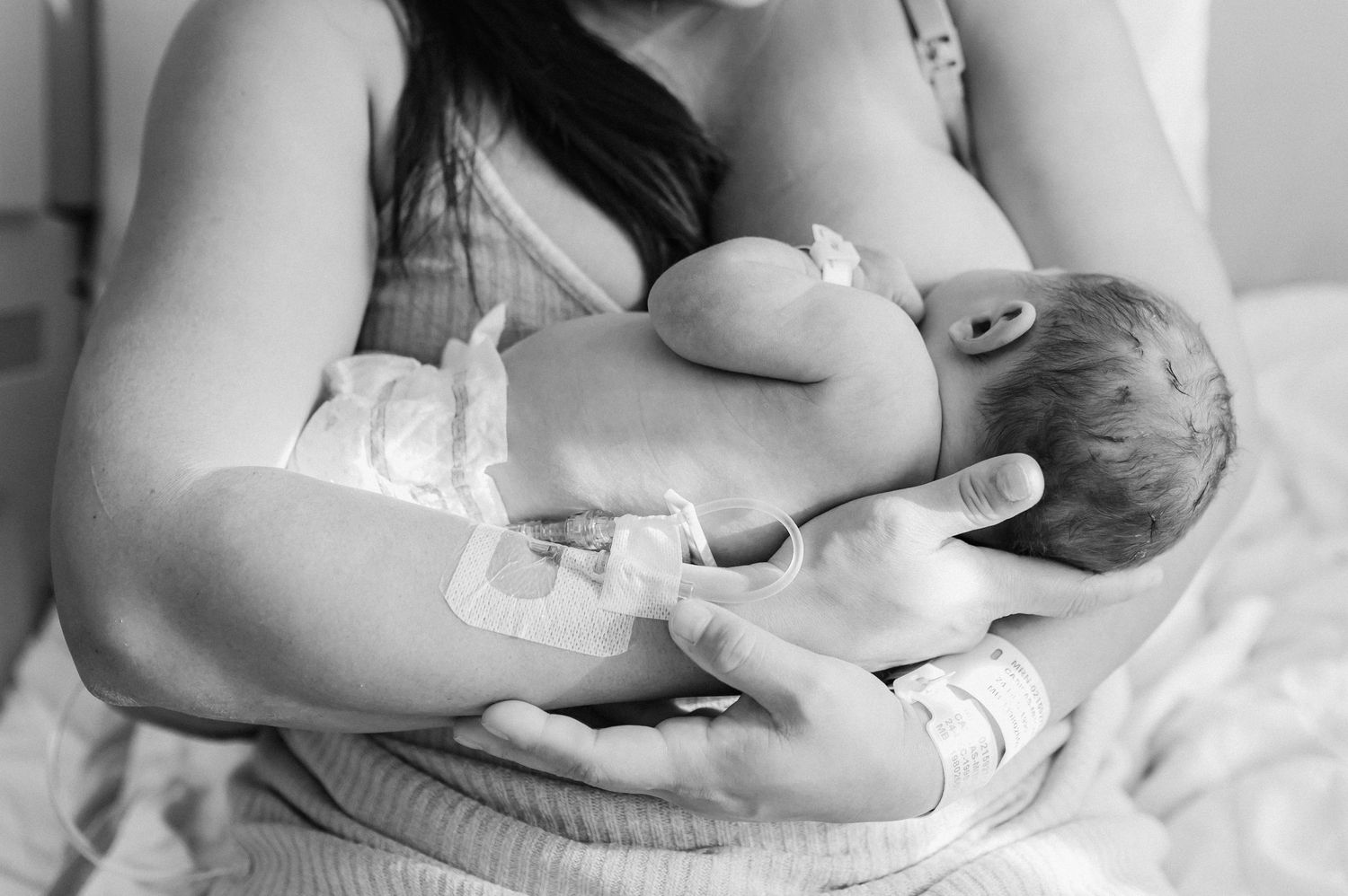 A tender moment captured in black and white as a parent cradles and nurses their newborn baby.