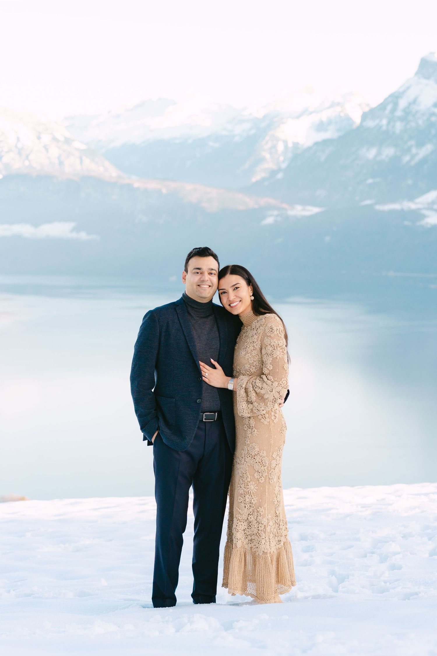 A couple shares a romantic moment on a meadow at Villa Honegg with mountains in the background during an engagement photoshoot.