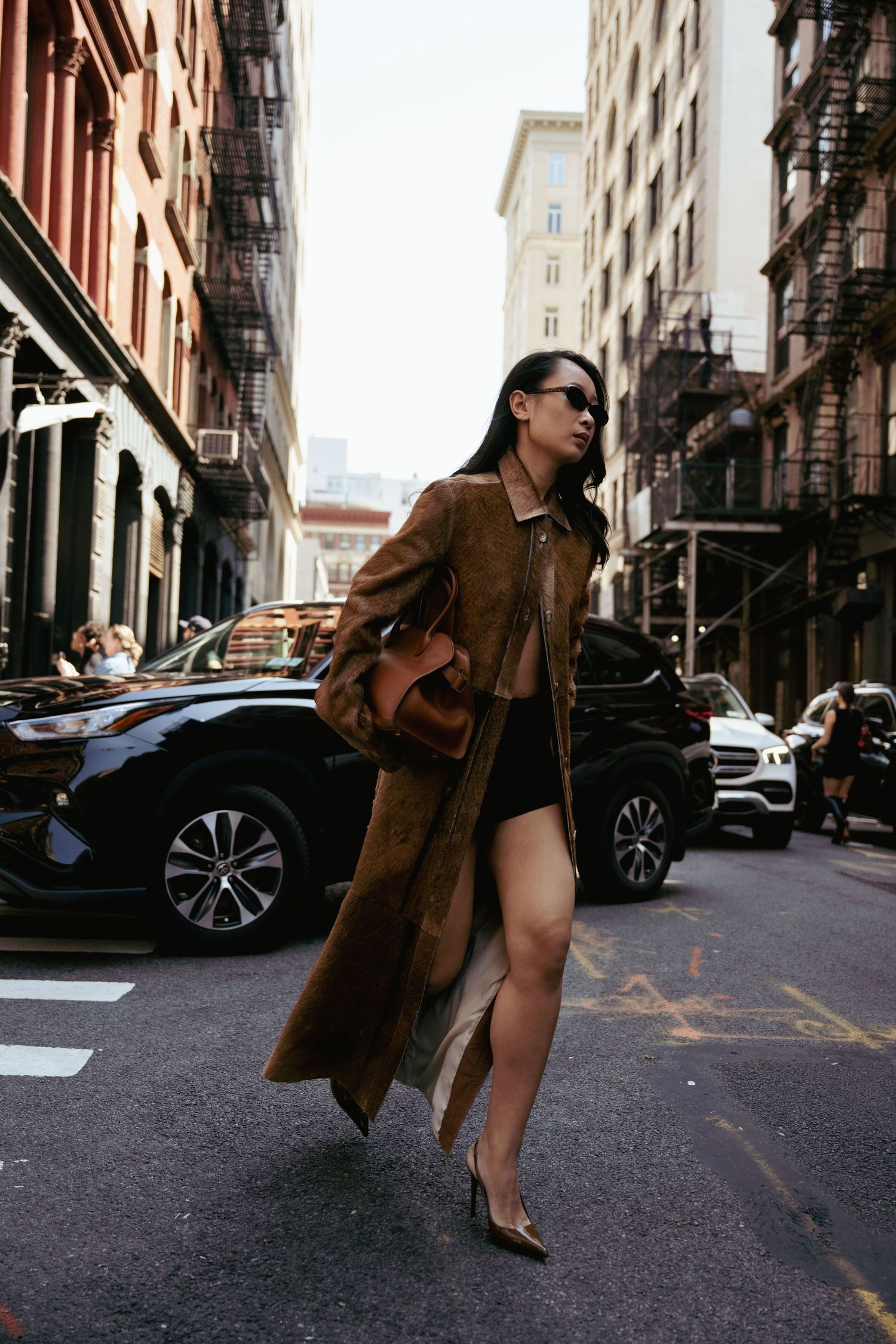 A fashion model poses on a city street wearing a brown trench coat and heels in a dynamic photo series.