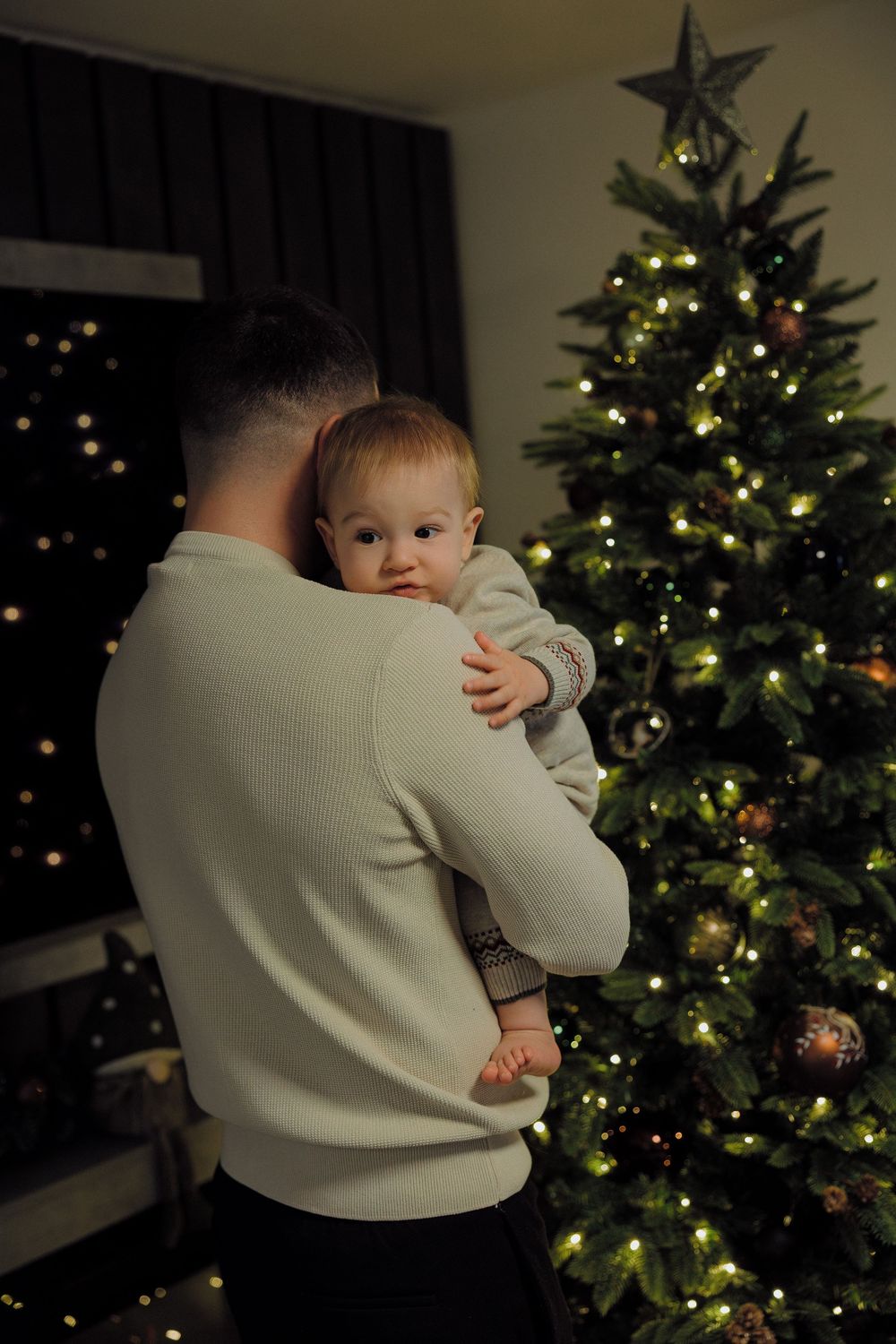 A series of photos showing a baby being held in front of a decorated Christmas tree with glowing lights in a dark room.