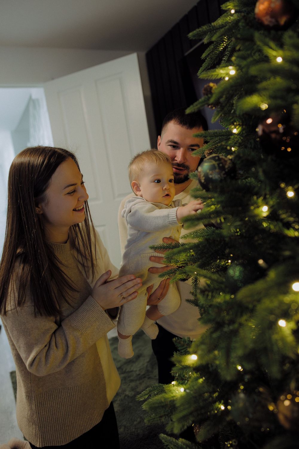 Family decorating Christmas tree together with warm lights glowing in a cozy home setting.