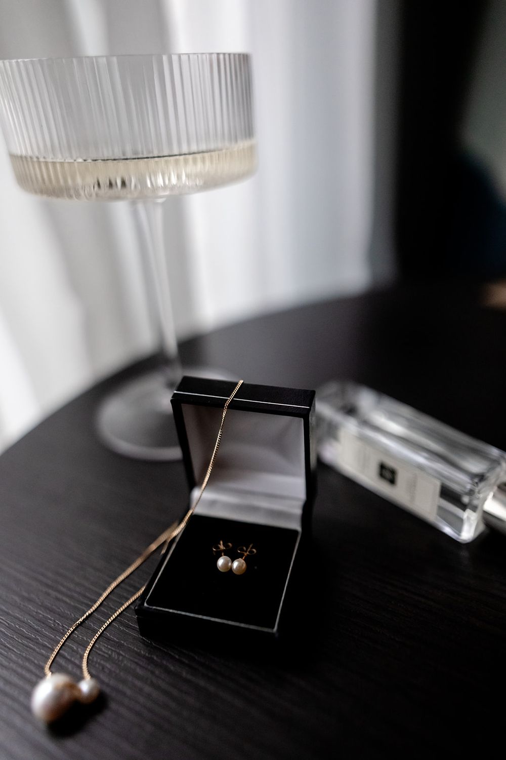 Pearl earrings and black jewelry box displayed on dark wooden surface with glass decor.