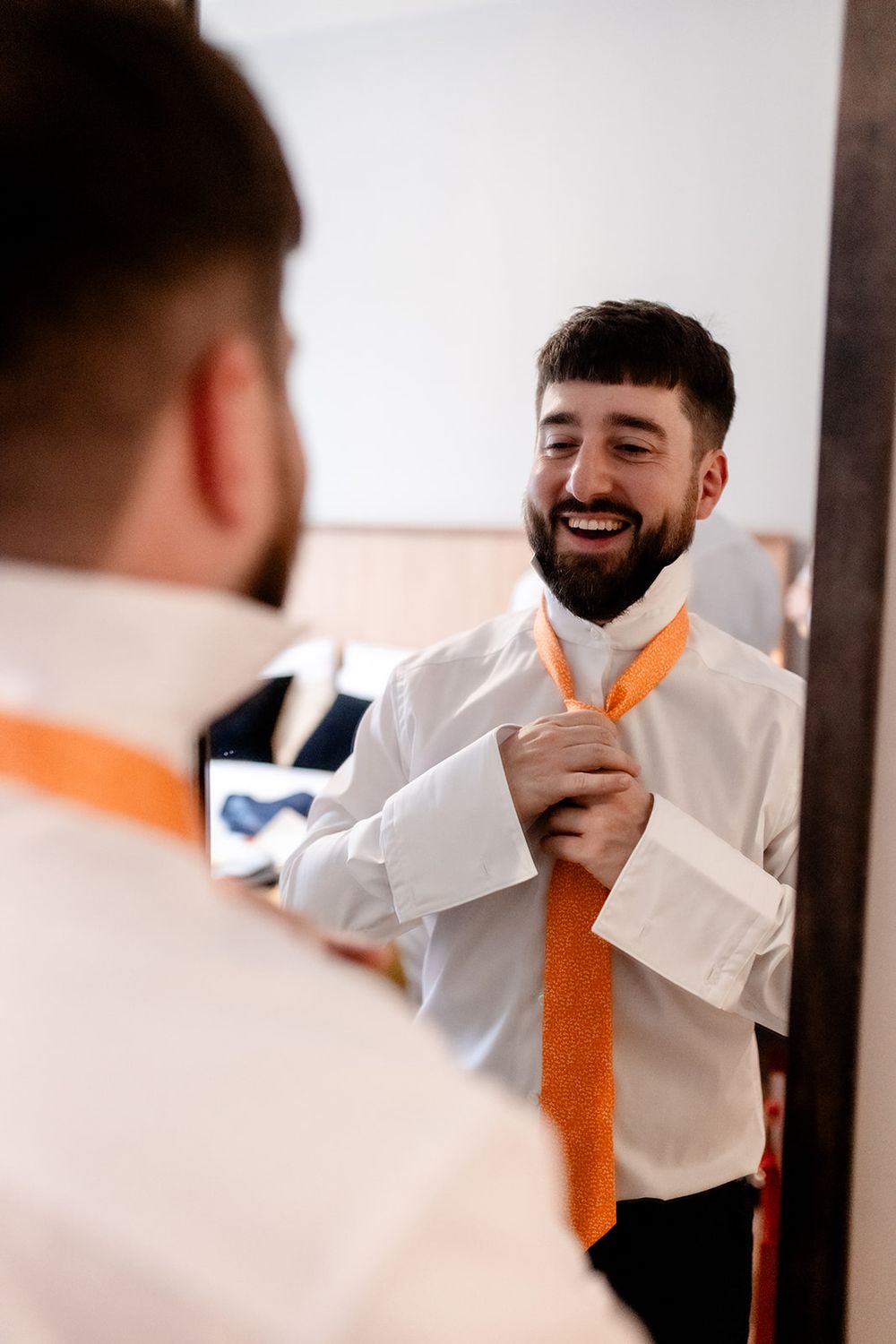 Man in white shirt and orange tie laughing while looking in mirror.