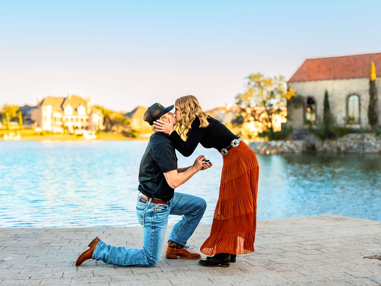 A couple shares a romantic moment together on a sandy beach at sunset with ocean waves in the background.