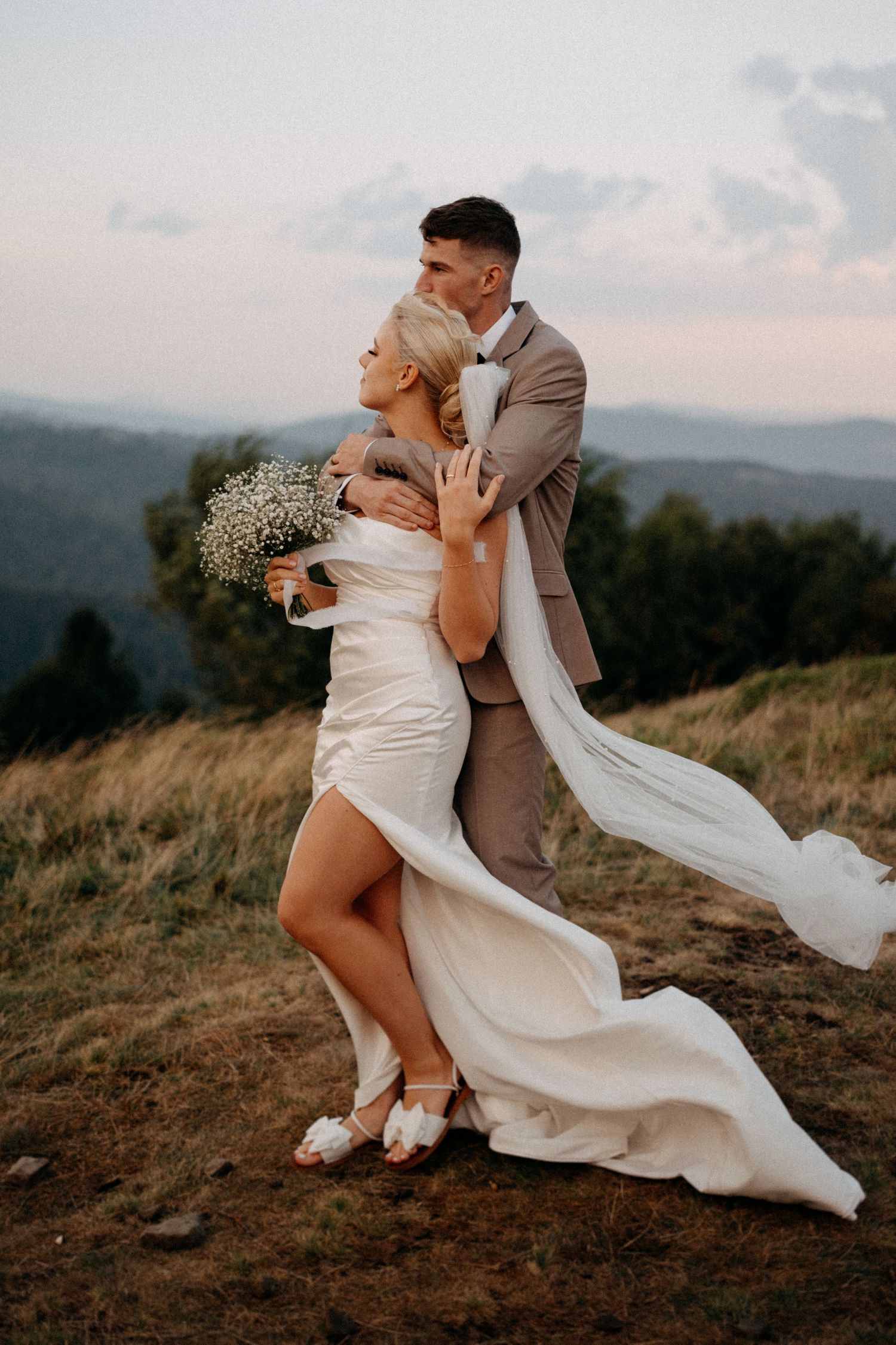 A dramatic wedding photo session on a hilltop with flowing dress and veil catching the mountain breeze.