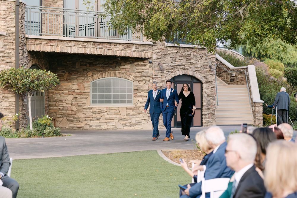 Wedding guests gather under an elegant stone archway during an outdoor ceremony celebration.