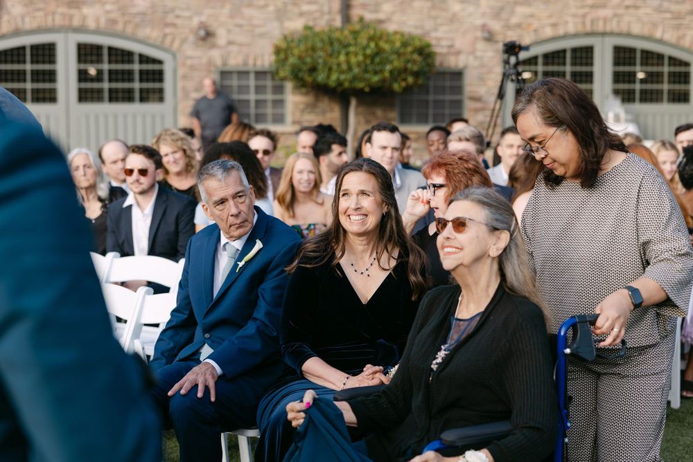 Wedding guests laugh and share joyful moments during an outdoor celebration on a sunny day.