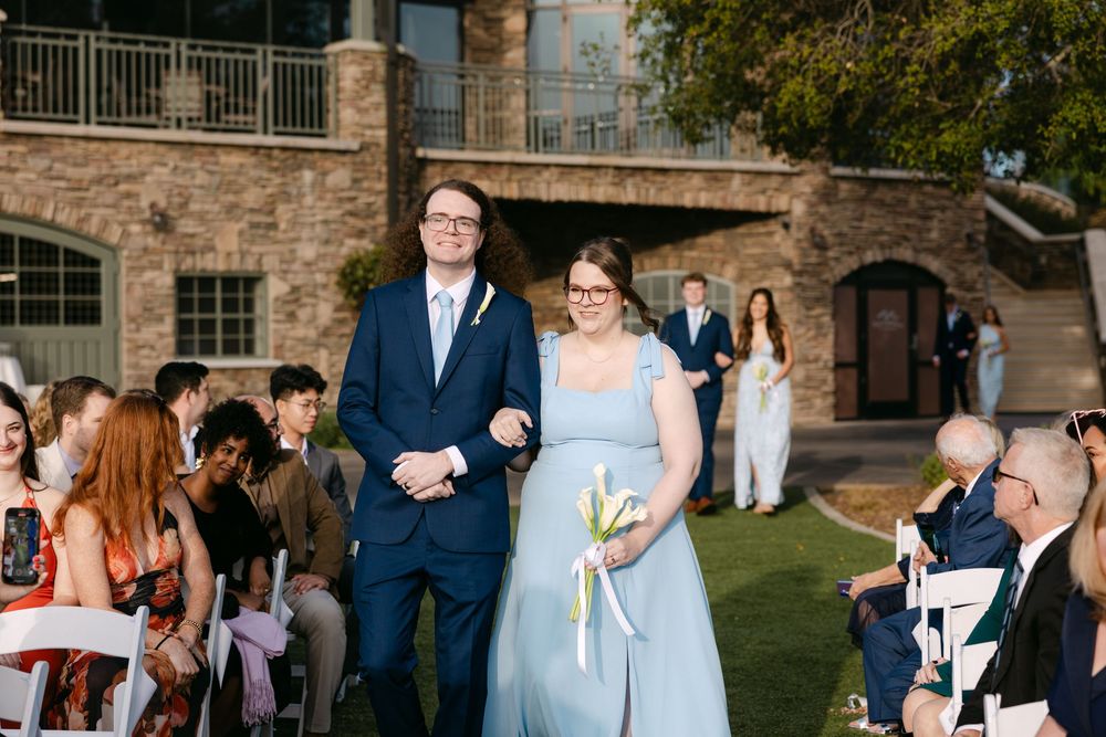 Guests mingle on a green lawn outside a stone building during a formal outdoor event.