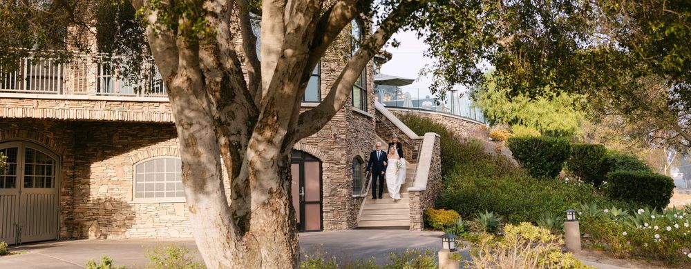 Stone walkway lined with trees and rustic buildings leads to a charming outdoor courtyard area.