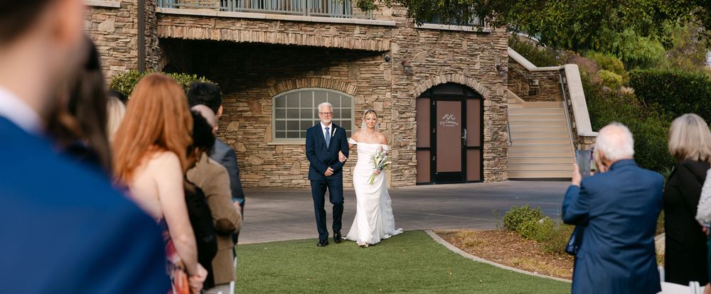Wedding celebration taking place in an elegant outdoor garden setting with stone architecture.