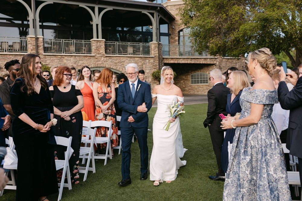 Wedding ceremony setup with white chairs on grass lawn against backdrop of stone building.