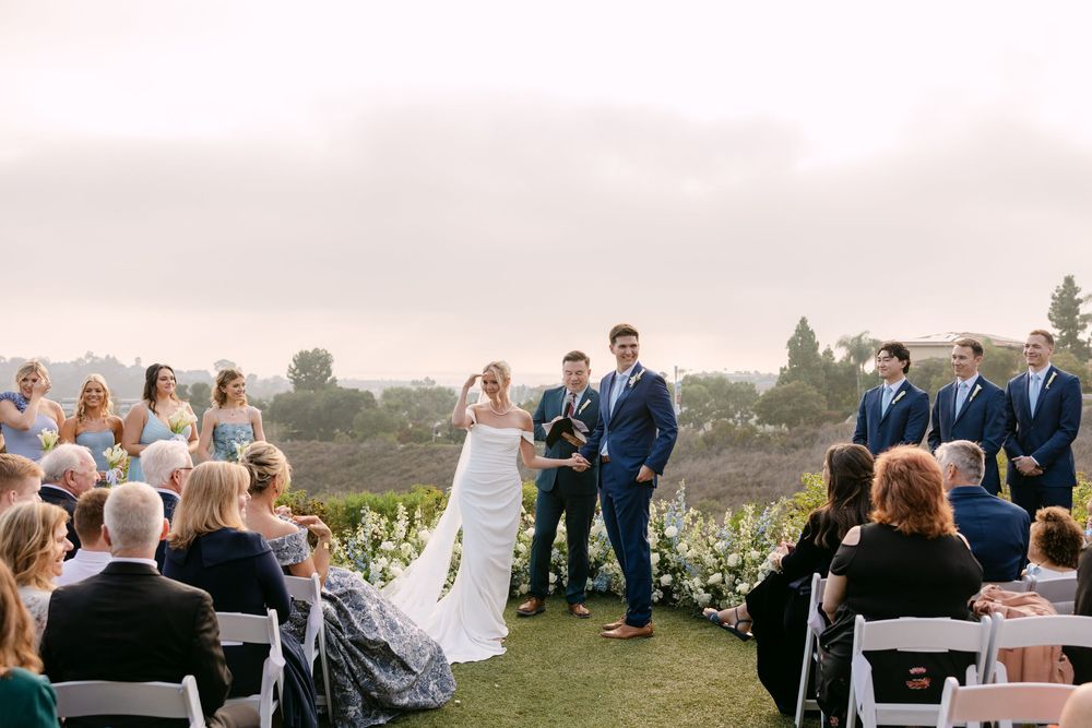 Panoramic view of wedding guests seated for an outdoor hilltop ceremony with mountain vistas.