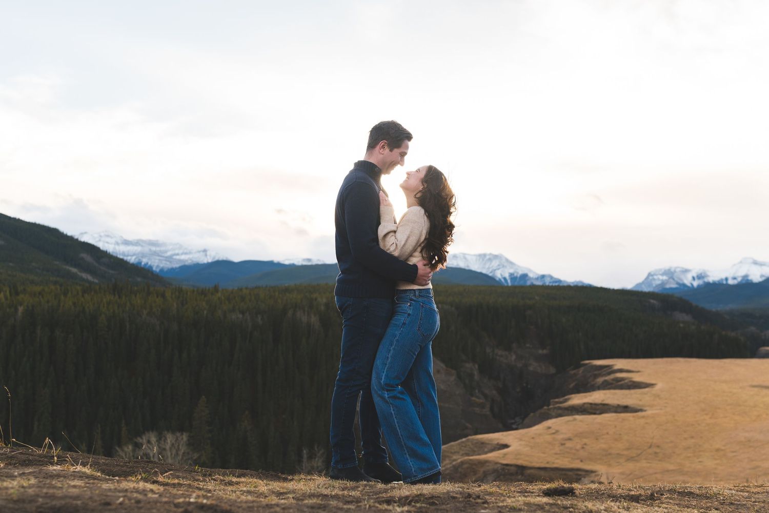 Couple embracing on hilltop with dramatic mountain vista behind them.
