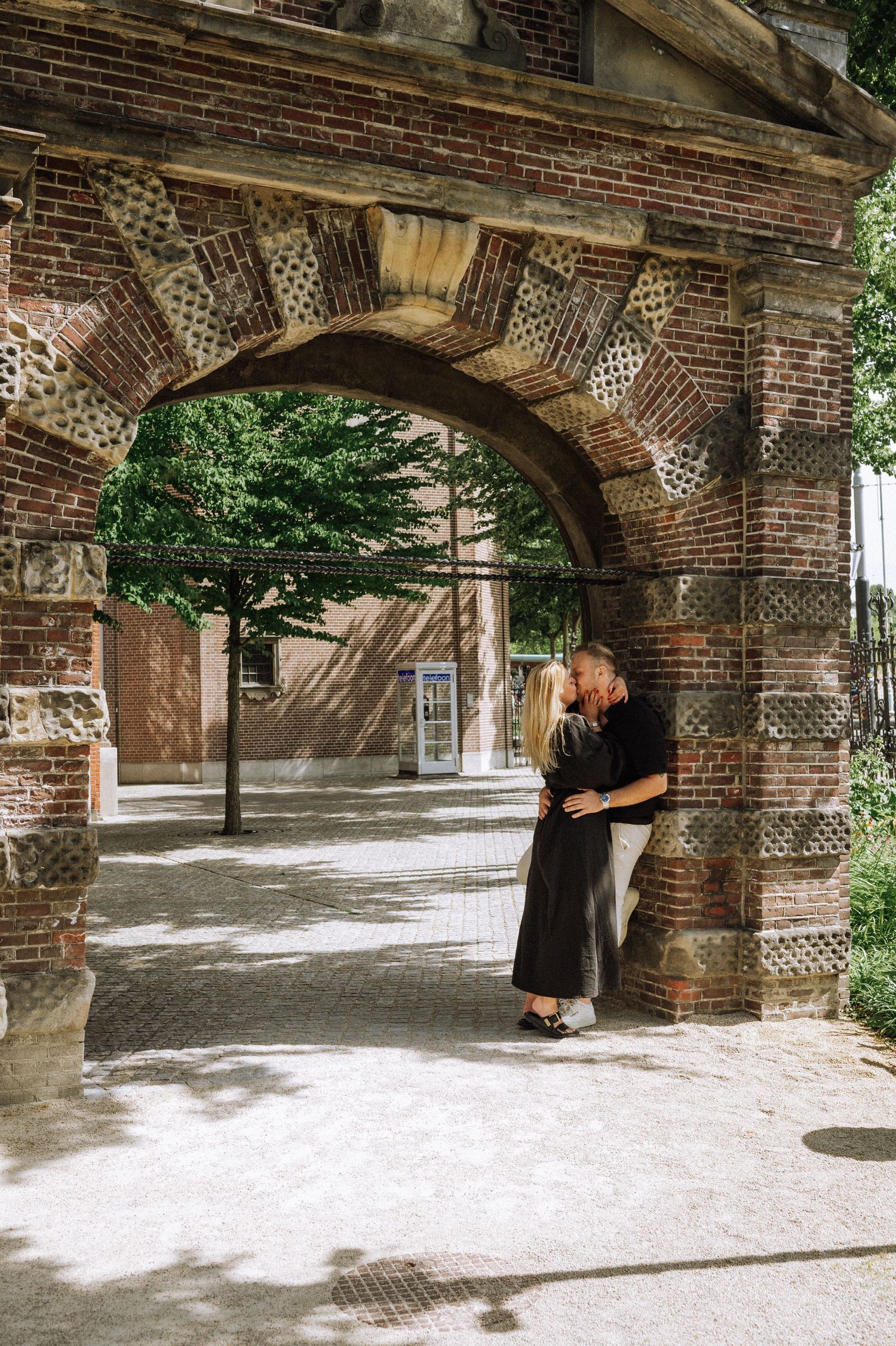 Couple embracing under a historic brick archway in a quiet part of the Rijkmuseum garden, Amsterdam